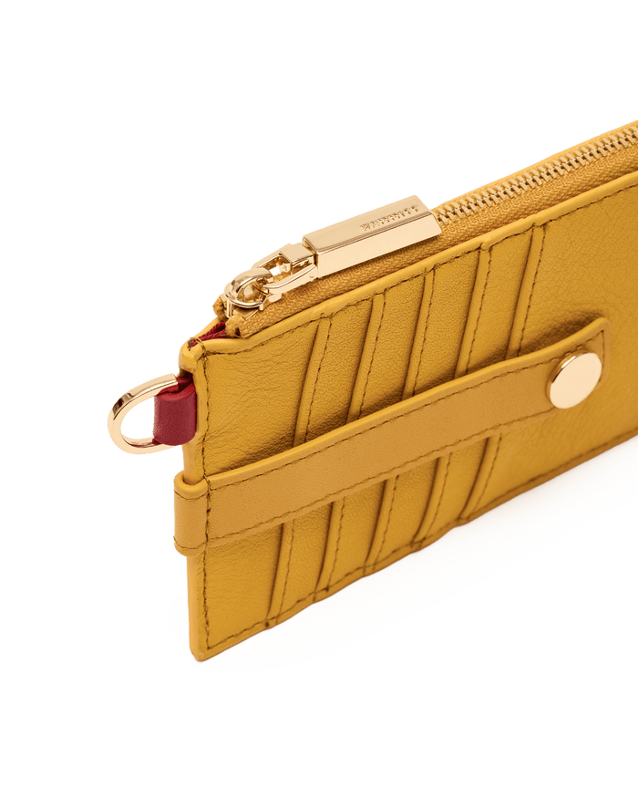 A close-up of a mustard yellow leather zip-around wallet or card holder with gold-tone hardware, a horizontal strap with a snap button, and a small burgundy ring accent, shown on a white background.