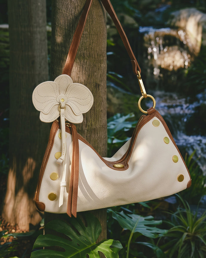 White handbag with brown accents and a floral keychain in a natural setting