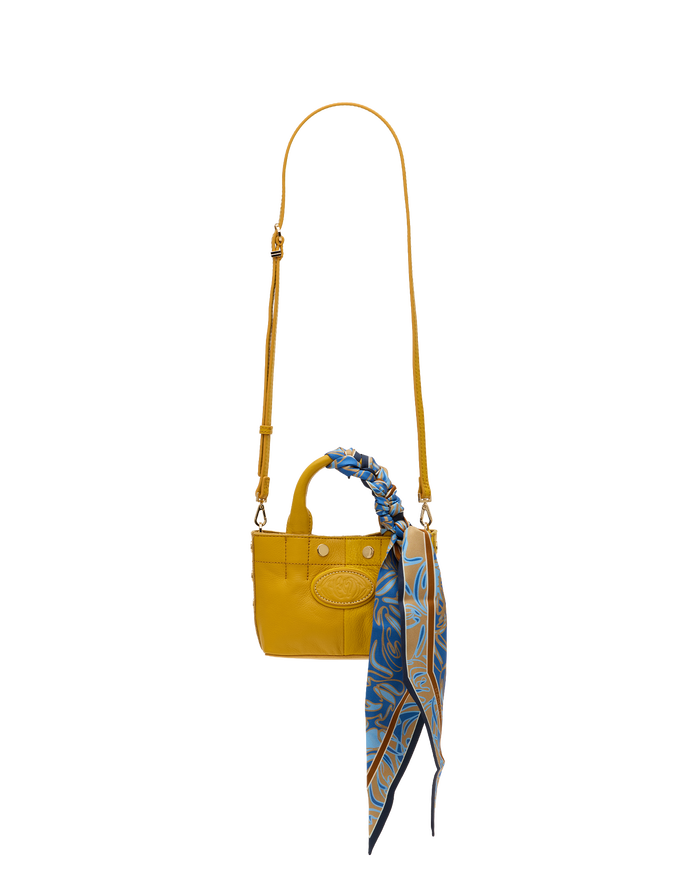 A small yellow leather handbag with a long shoulder strap, top handles, and a blue patterned scarf tied to the handle, shown against a plain white background.