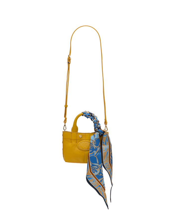 A small yellow leather handbag with a long shoulder strap and a blue patterned silk scarf tied to the top handle, shown against a plain white background.