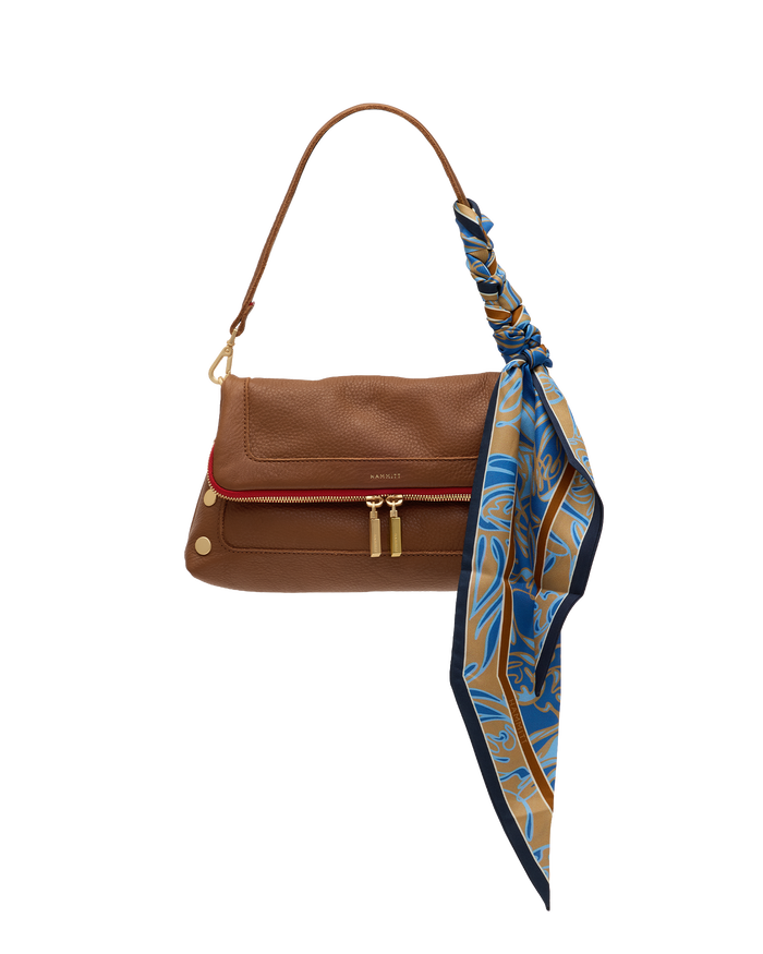 A brown leather shoulder bag with a red accent stripe along the front zipper, gold-tone hardware, and a blue, gold, and navy patterned silk scarf tied to the strap, shown on a plain white background.
