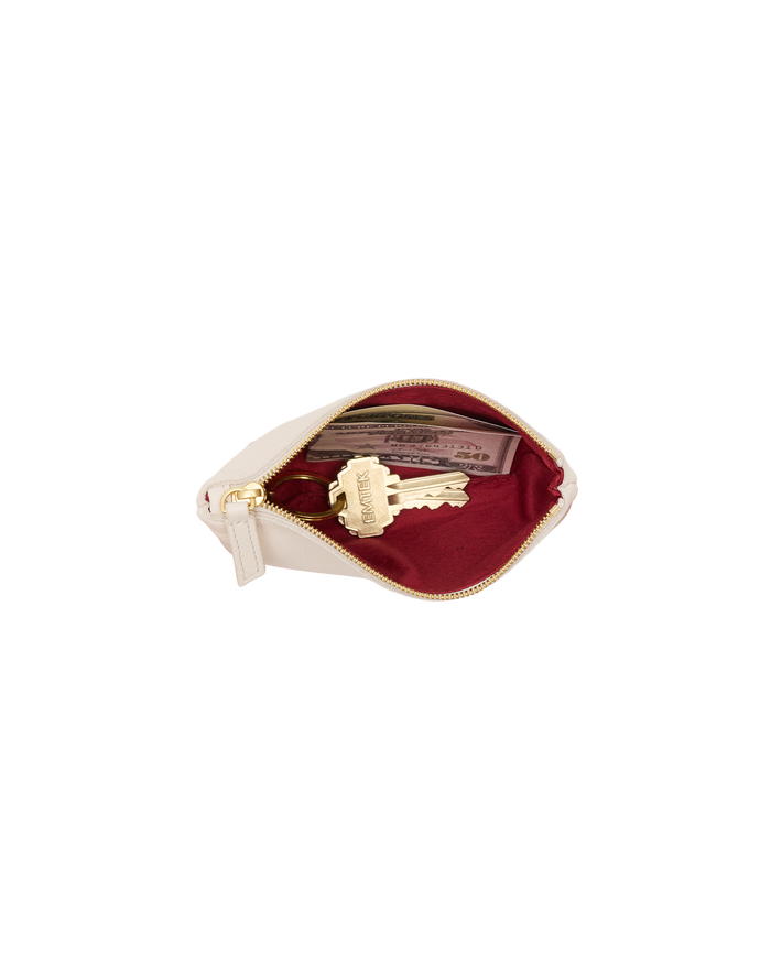 A cream-colored leather key pouch with a gold zipper, shown open to reveal a deep burgundy velvet interior containing a gold key and a card.